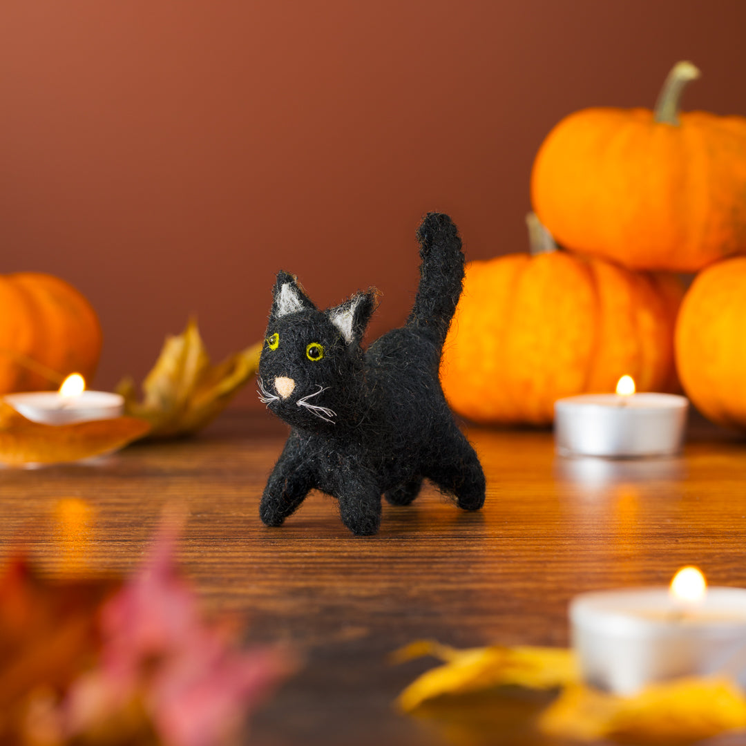 Black cat figurine on a wooden table with pumpkins and candles in the background
